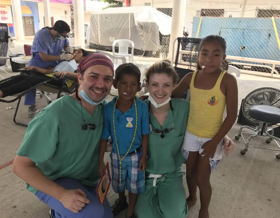 Two volunteers in scrubs with two local children at the 2017 clinic.